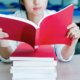 young woman reading a red book on a stack of other red books